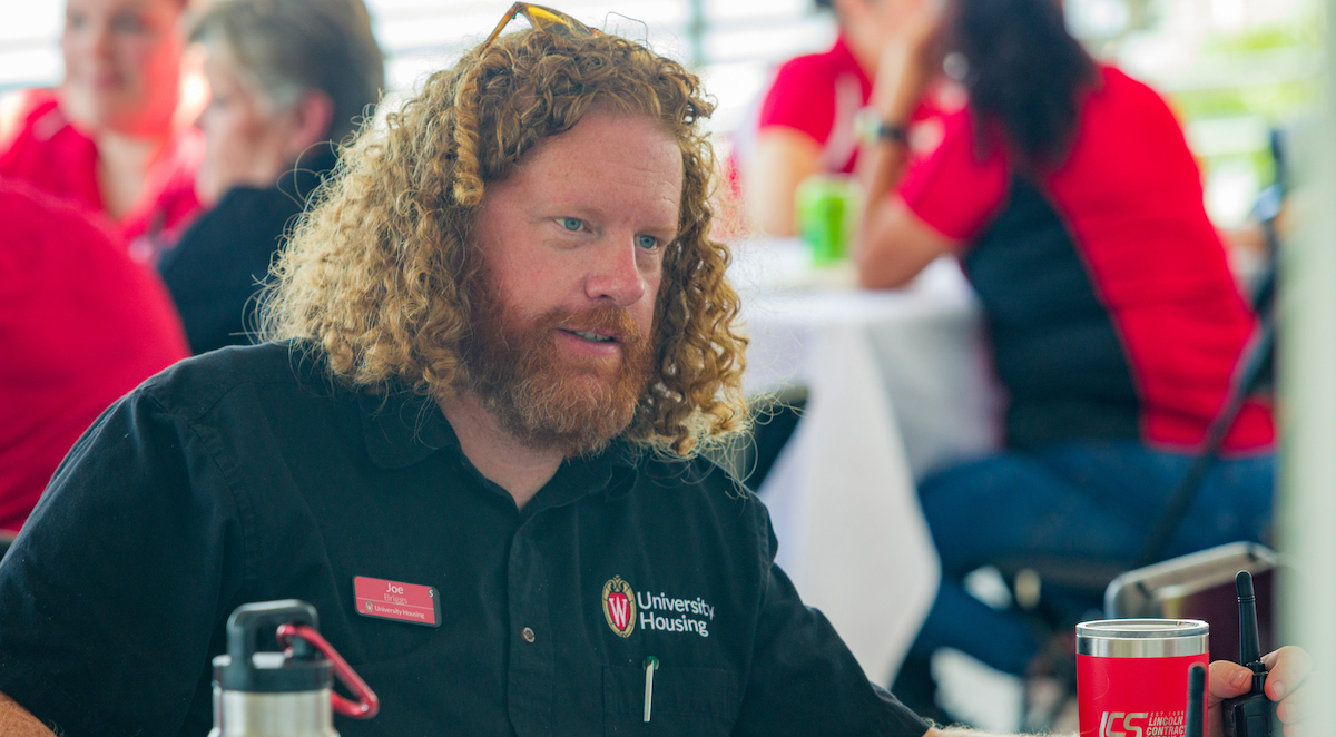 A staff member with curly red hair in a black shirt interacts with other staff