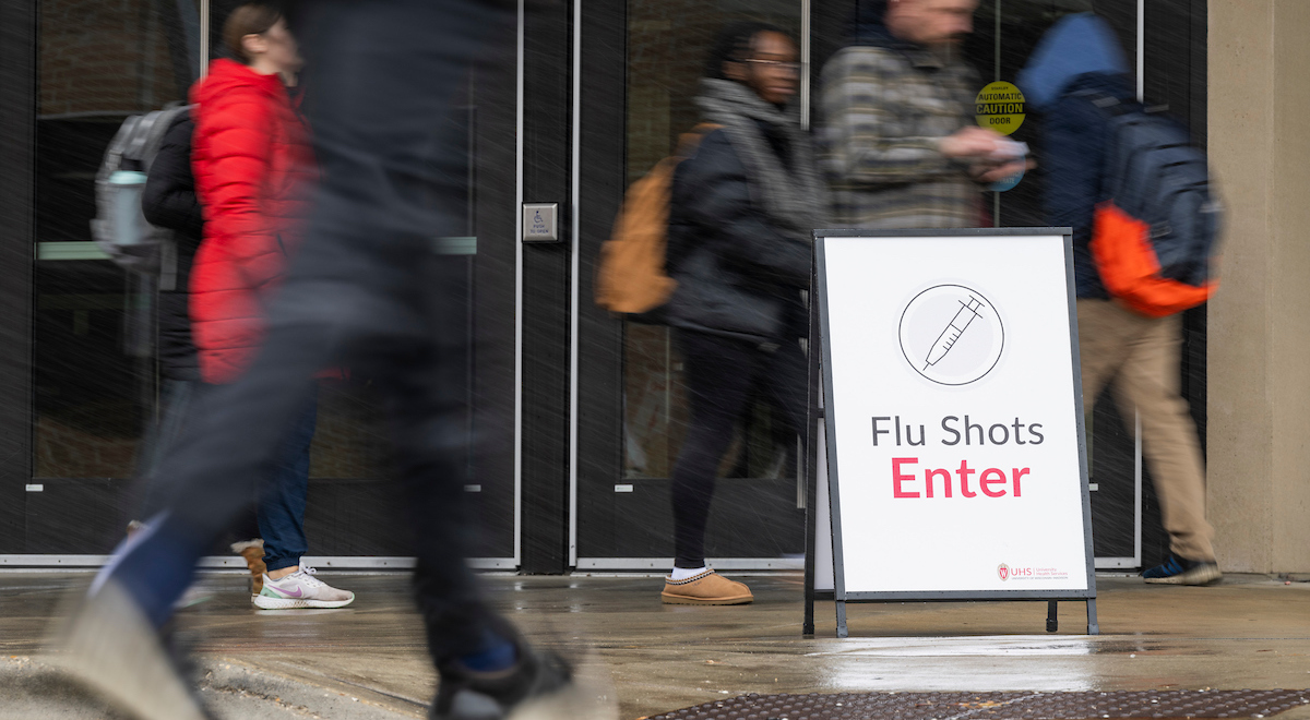 Students walking around an outdoor sign that reads "Flu Shots - Enter"