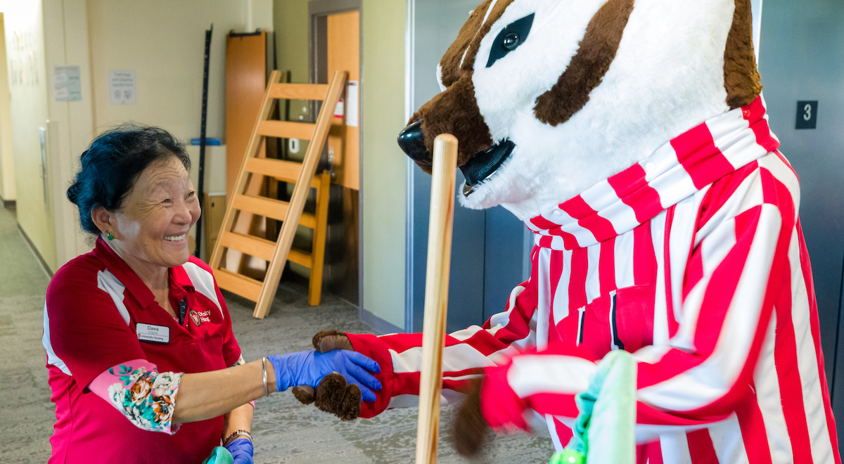 A Facilities staff member shaking hands with Bucky Badger on a Dejope Residence Hall floor