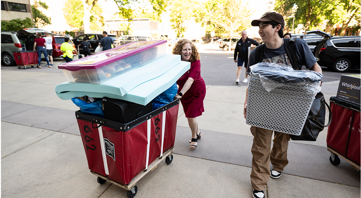 Chancellor Moonkin pushing red cart with student