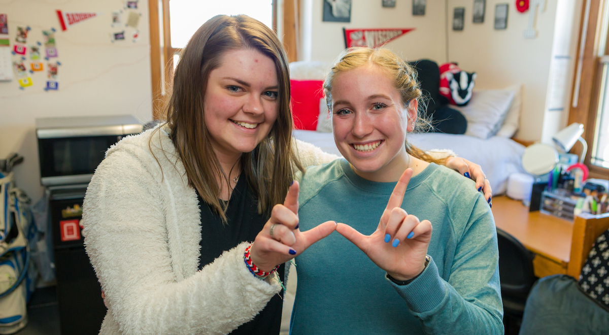 Two students make a "W-hands" gesture in their decorated residence hall room