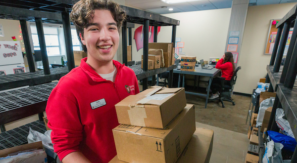 A University Housing student employee holding cardboard boxes at the Lakeshore Package Center