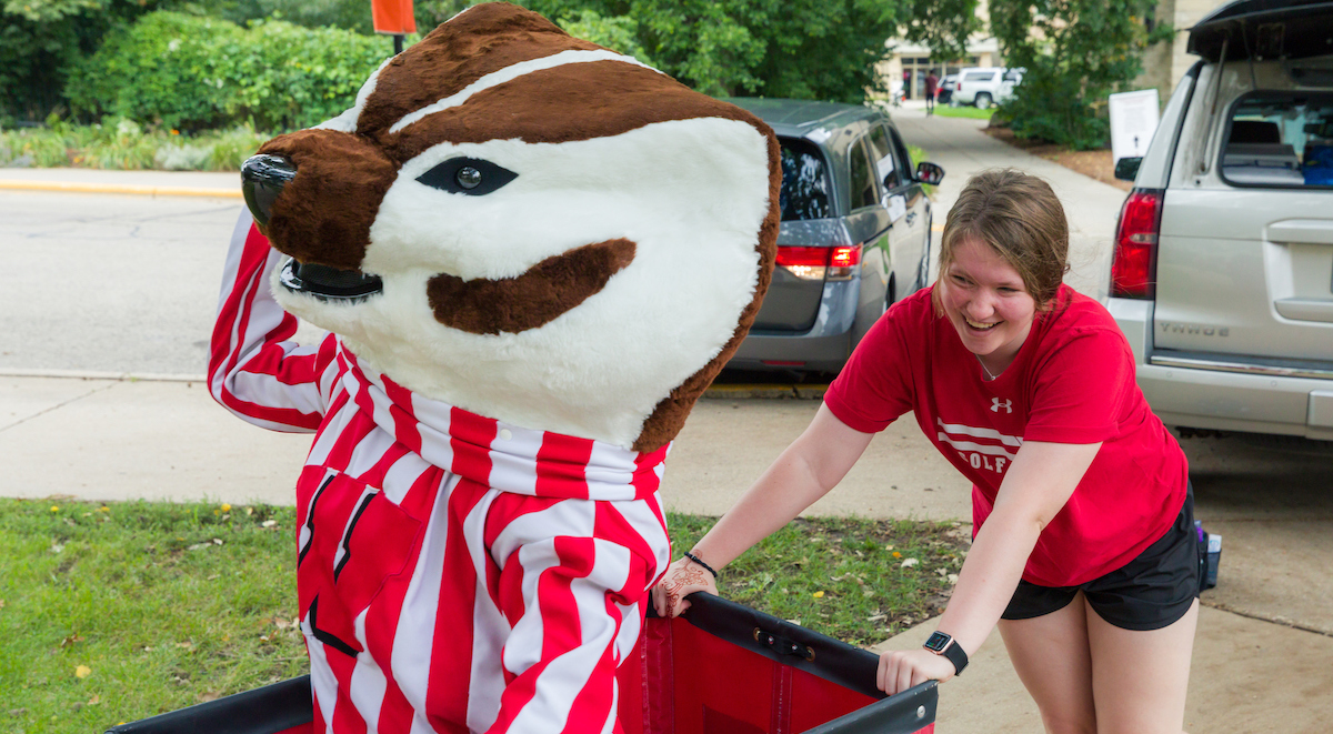 A new Badger student pushes Bucky Badger in a red cart during move-in