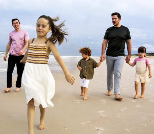 Two men walking with their kids on a beach