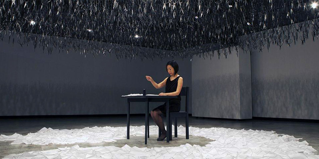 Woman sits at a table in an art installation.