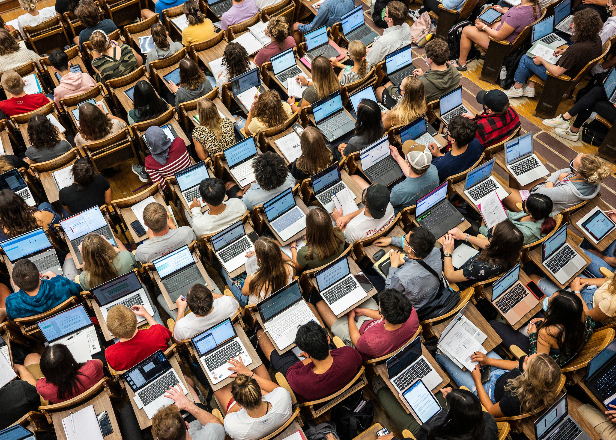 An overhead shot of students in a lecture hall taking notes on their laptops.