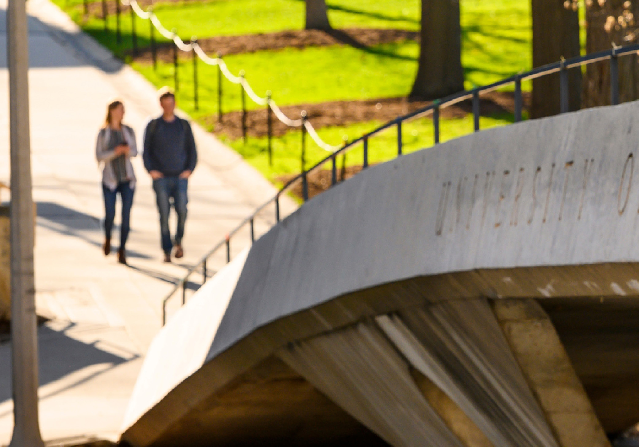 Two people walk down a paved sidewalk toward a concrete bridge.