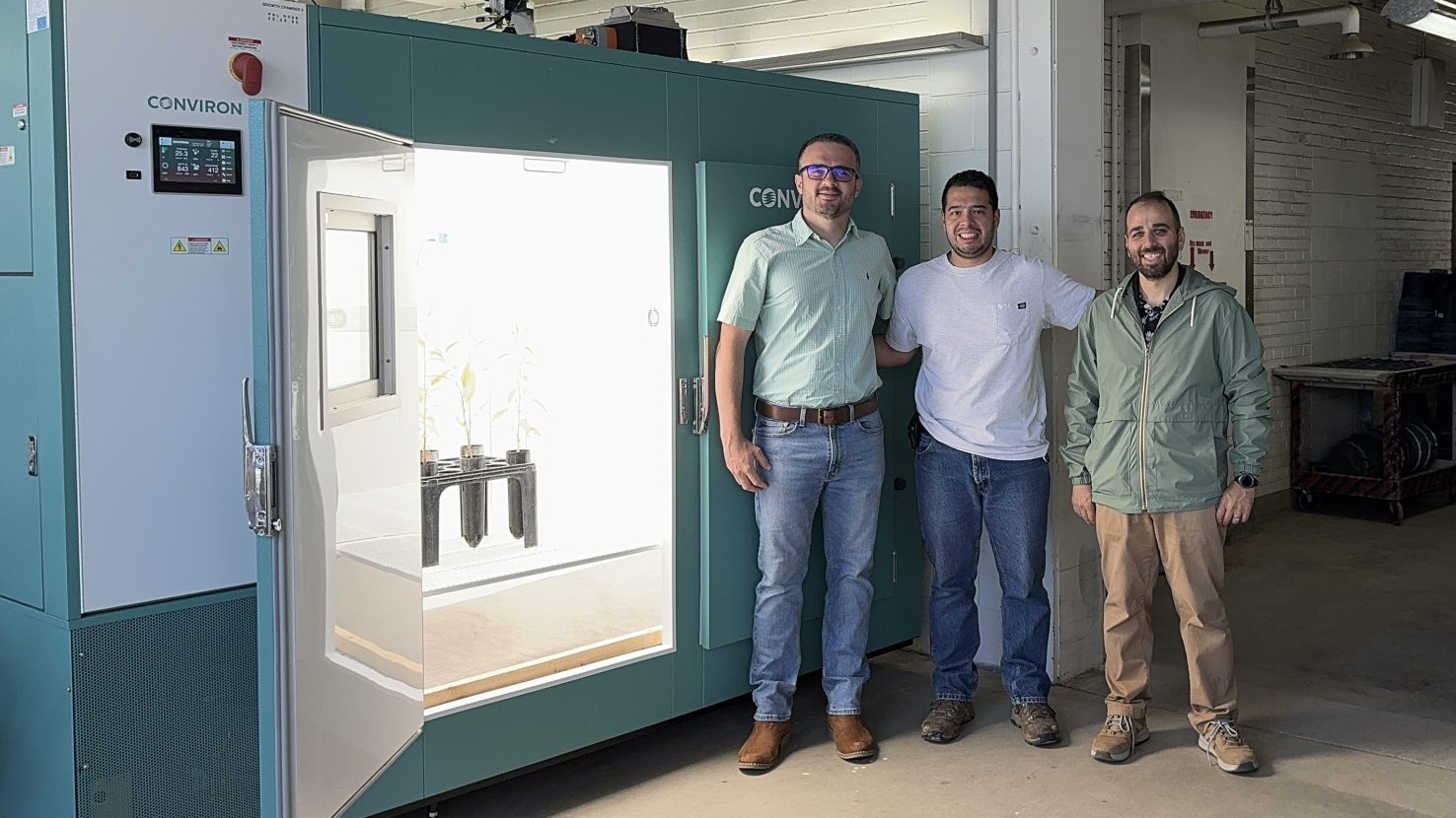 Three people pose and smile for a picture next to a large plant growth chamber.