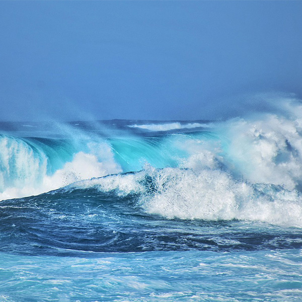 Crashing waves of an ocean against a blue sky.