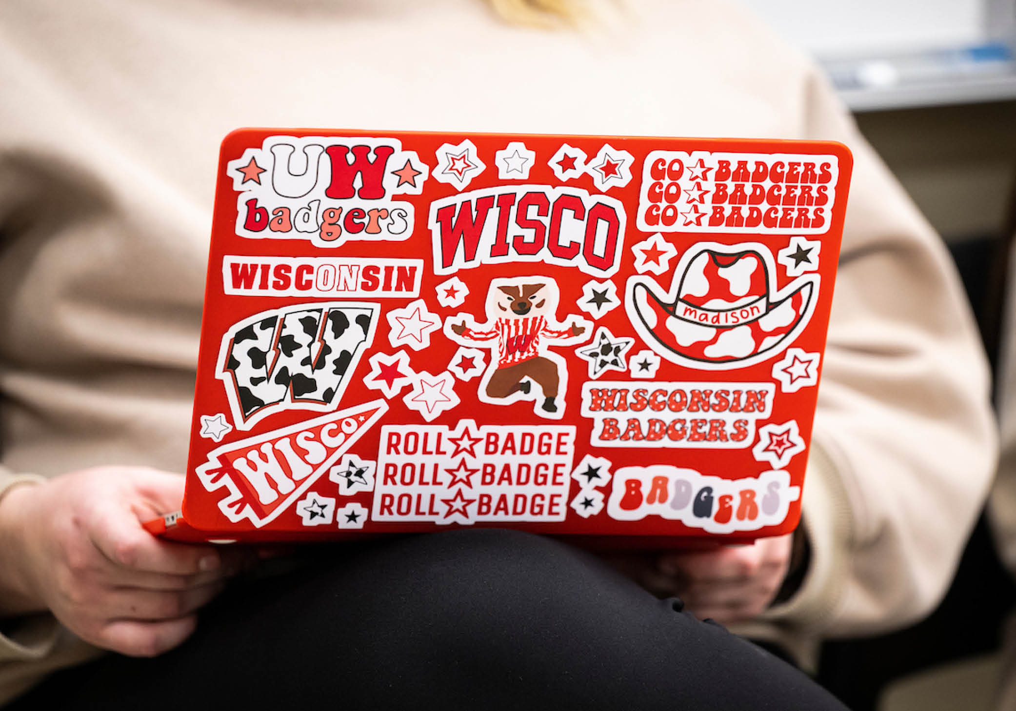 A person holds a laptop decorated with UW-themed stickers on their lap.