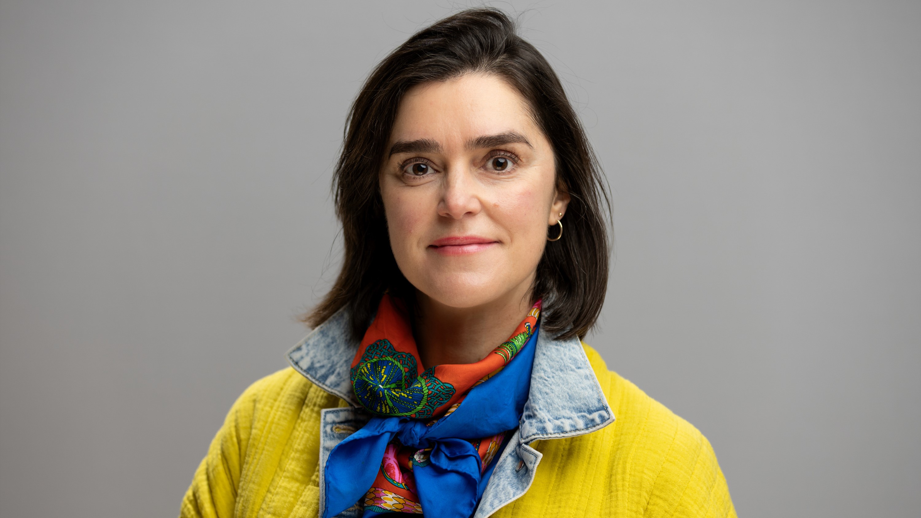 Amaya Atucha smiles for a professional photo. She wears bright yellow and blue.