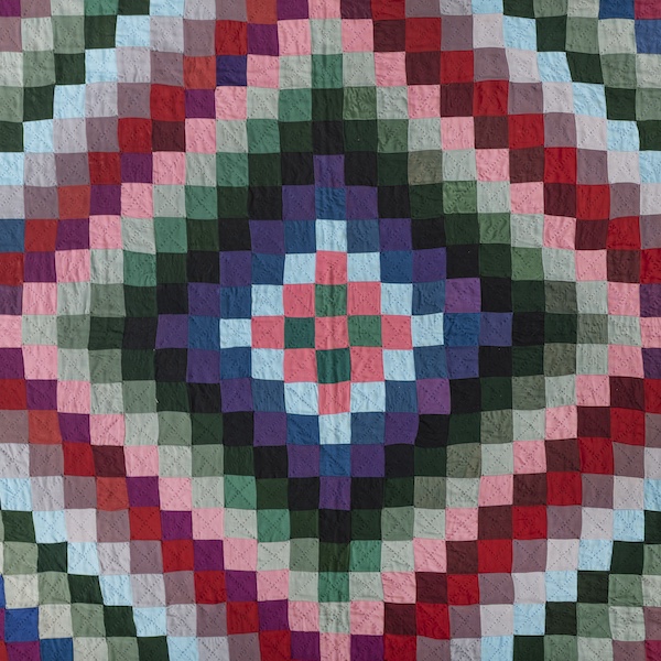 A close cropped view of a geometric quilt with radiating blocks of blue, pink, green, and purple creating an optical effect.