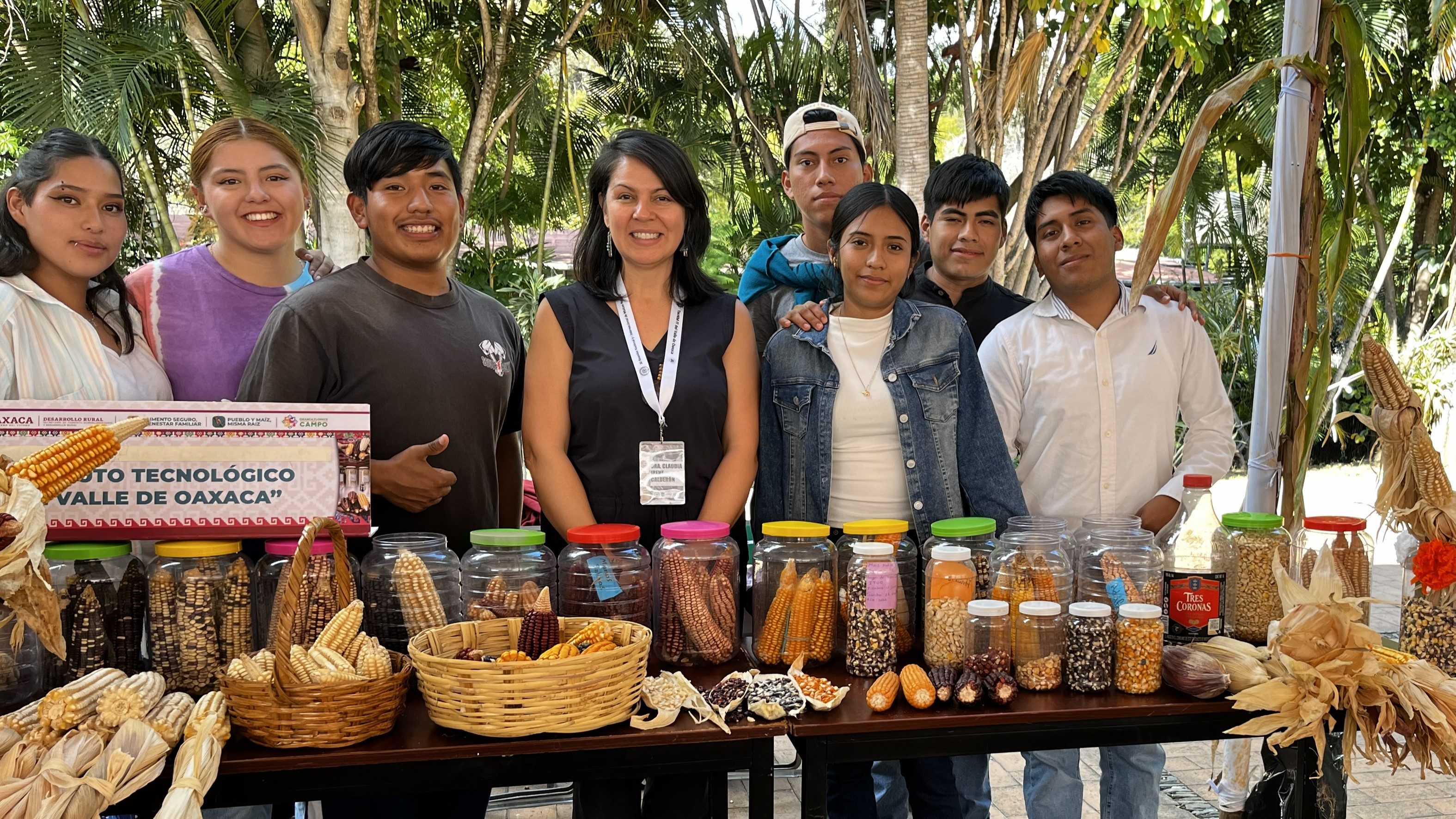 A group of people smile for a picture behind a booth that displays many different maize varieties.