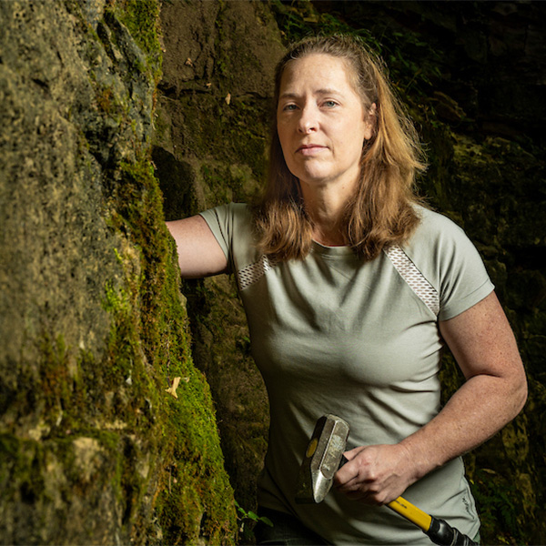 Andrea Dutton posing near mossy rockwall. 