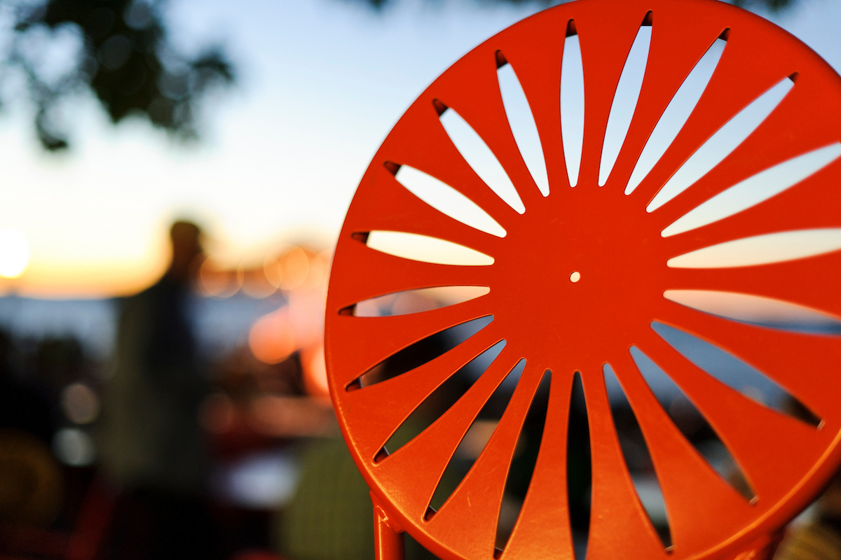 Close up of red-orange chair with a blurred sunset behind it