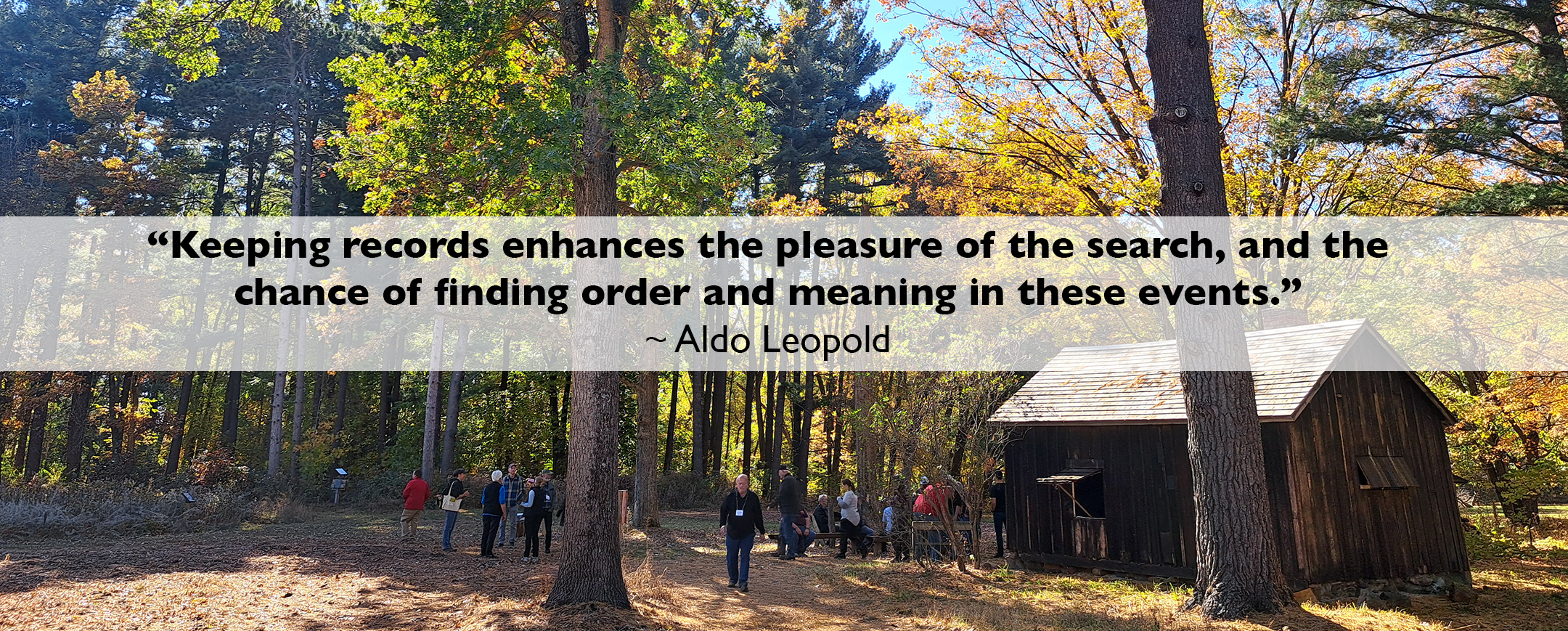 wide angle of the Aldo Leopold Shack in Baraboo during fall with several people standing among the trees.