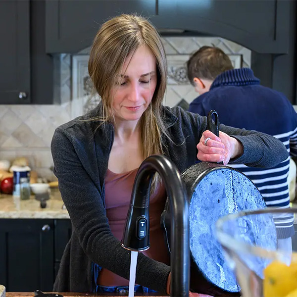 Jessica Calaro cleaning dishes at kitchen sick as family members help in background.