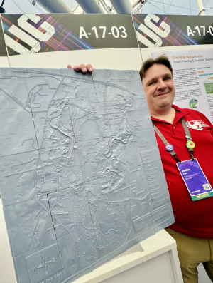 A smiling man stands next to a large gray relief map