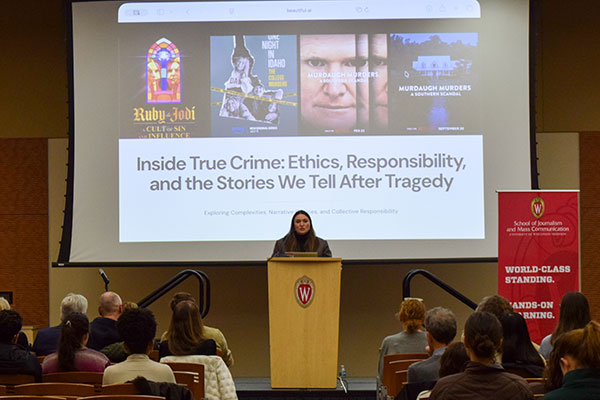 A woman speaks at a podium on a stage in front of a screen that reads "Inside True Crime: Ethics, Responsibility and the Stories We Tell After Tragedy"