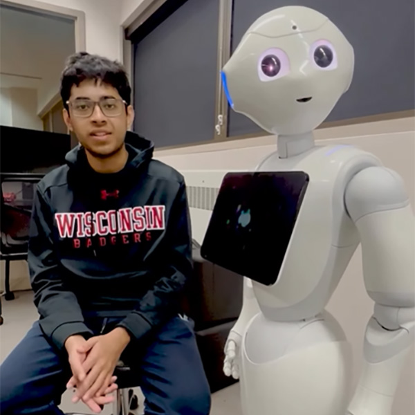 LASER researcher Manas Joshi speaking while sitting next to AI robot.