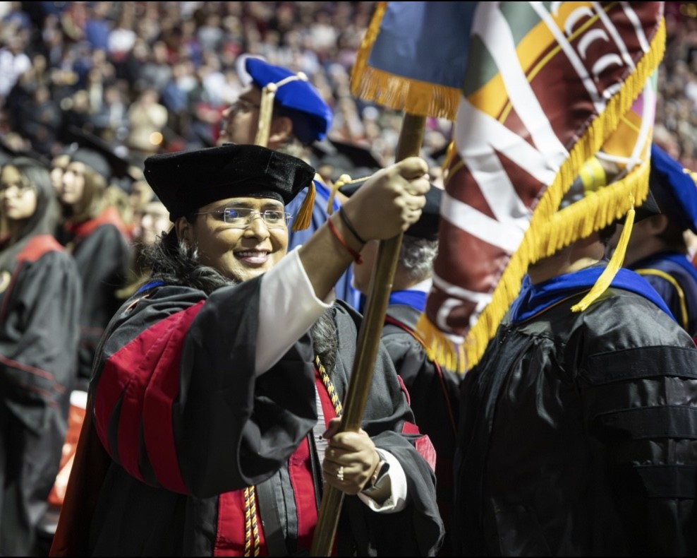 Dharani Suresh Babu smiles and carries a flag at commencement.