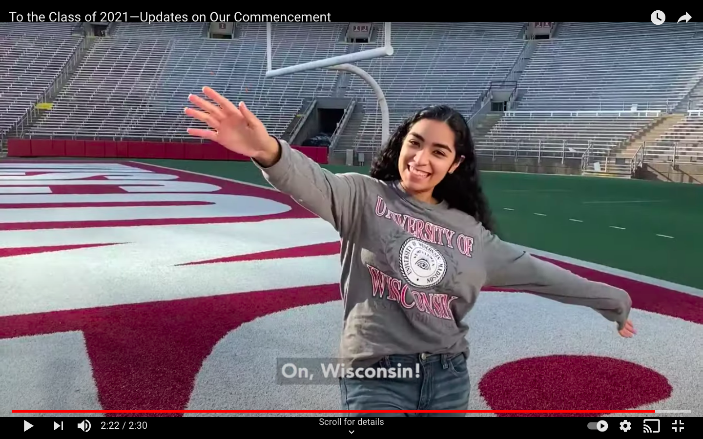 A screenshot of a YouTube video where a girl smiles and stands with her arms outstretched on the field of Camp Randall.