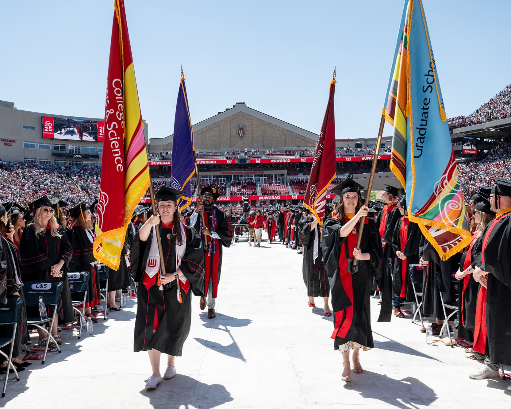 At Camp Randall Commencement, Jaya Hafner and other students carry flags.