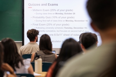 Students view a lecture slide labeled Quizzes and Exams describing assessments in the course