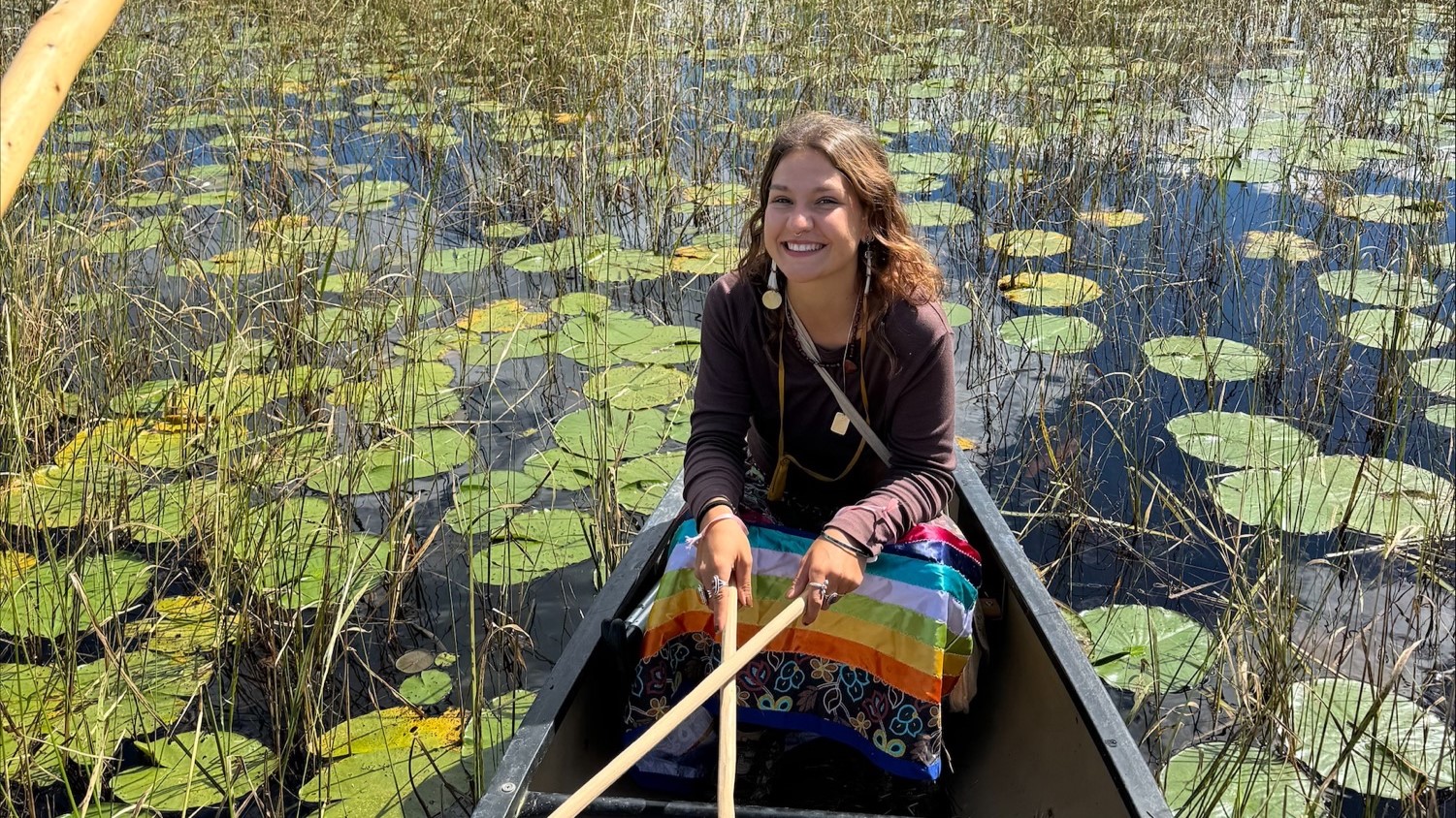 Sagen Lily Quale sits in a boat surrounded by water lillies and other aquatic plants.