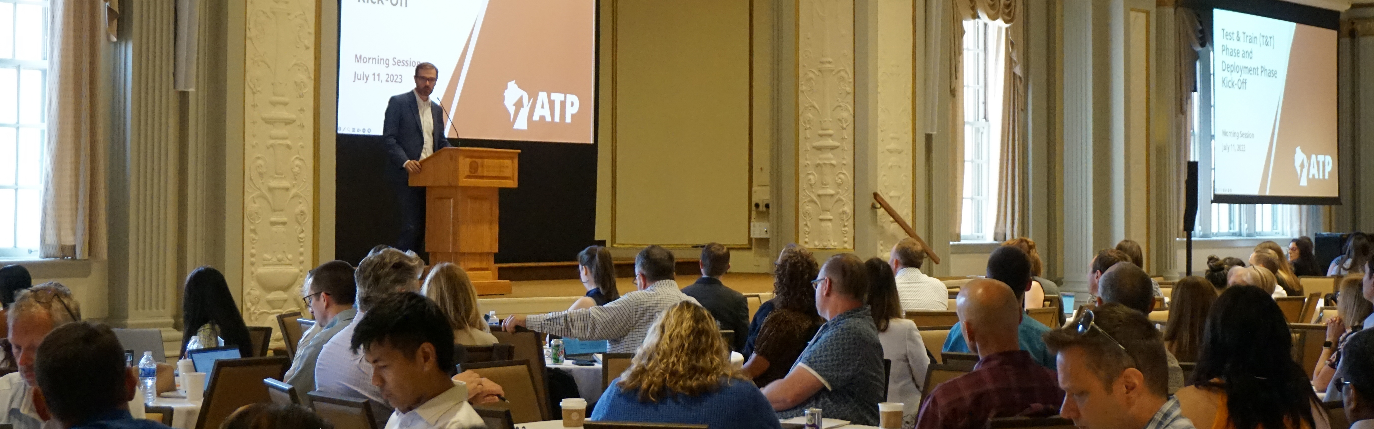 Steven Hopper, ATP Program Executive, presents from a podium in front of a room of ATP team members and stakeholders as part of the Test & Train kickoff in July 2023