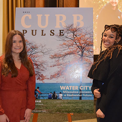 Two students pose next to a poster of Curb's newest issue, "Pulse"