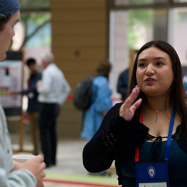 Alexandra Ugalde explaining research poster board to guest.