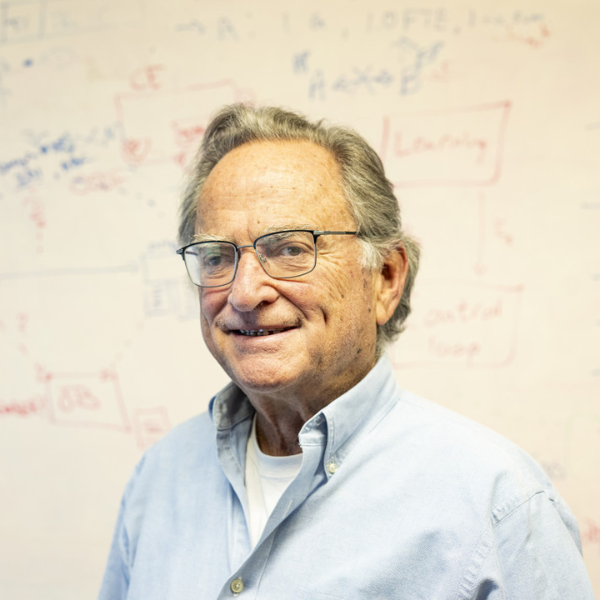 Miron Livny, in a blue shirt, stands before a whiteboard.