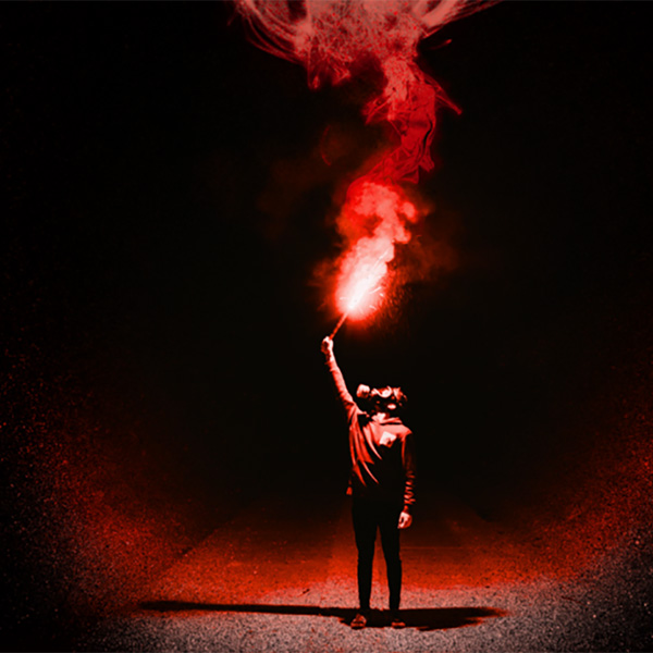 Person in gasmask holding a flare in air surrounded by darkness.