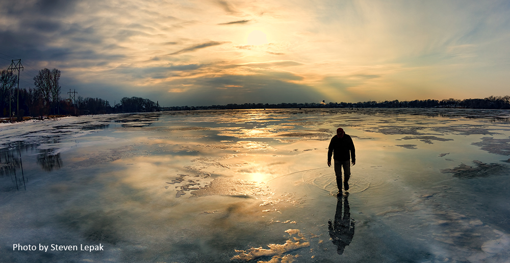 Silhouette of person walking on an ice-covered lake at dusk - photo by Steven Lepak