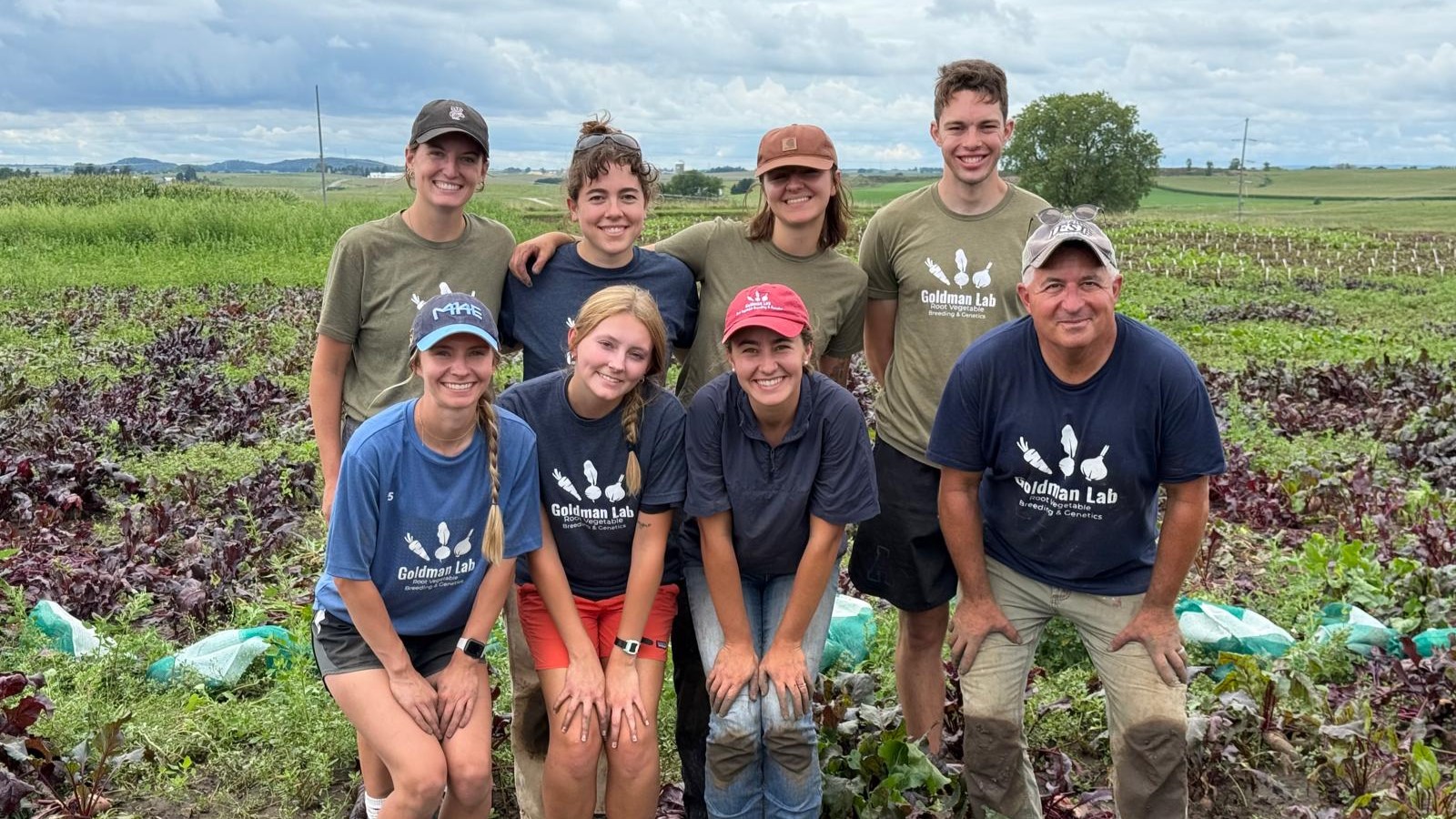 Two rows of people pose and smile for a picture in a field.