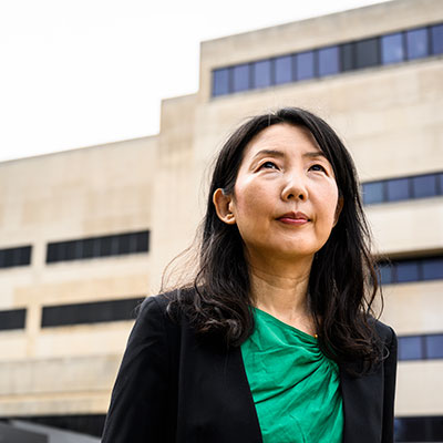 Headshot of Young Mie Kim in front of a tan building with her looking up to the sky