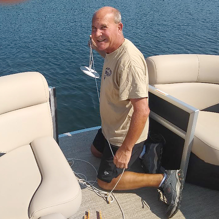 photo of a man kneeling in a pontoon boat on the water holding a Secchi disc for measuring water clarity